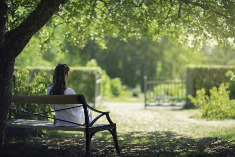 Dame sett bakfra på en benk i en park